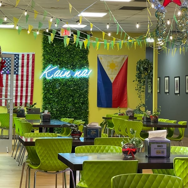 Maemax Market's dining area with lime green chairs, a neon "Kain na!" sign, and Filipino and American flags.
