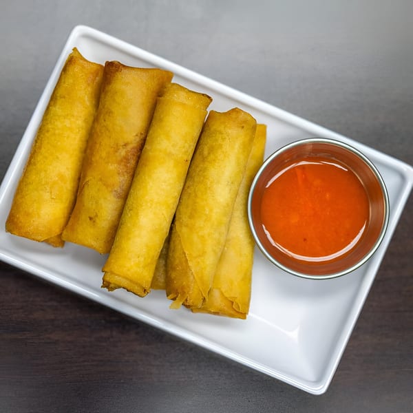Golden-fried Filipino lumpia spring rolls with a side of red dipping sauce on a white rectangular plate.