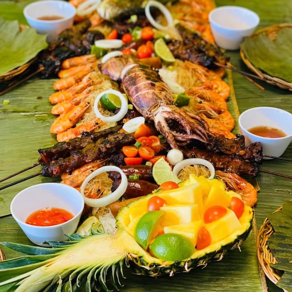 A Filipino boodle fight feast with grilled seafood, skewers, and fruit on banana leaves.