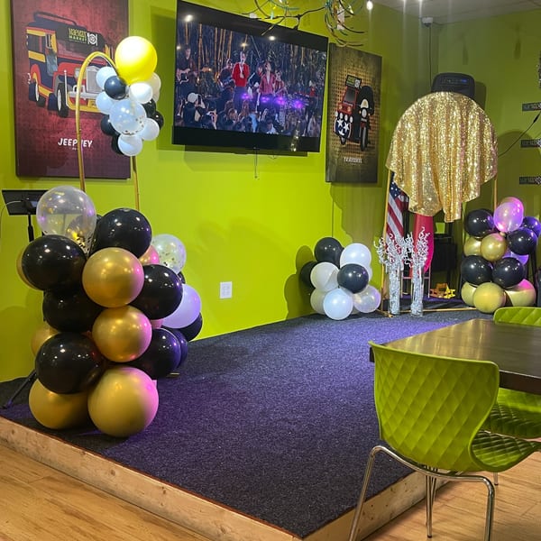 A vibrant green-walled room with a stage, balloons, and Filipino jeepney artwork at Maemax Market.