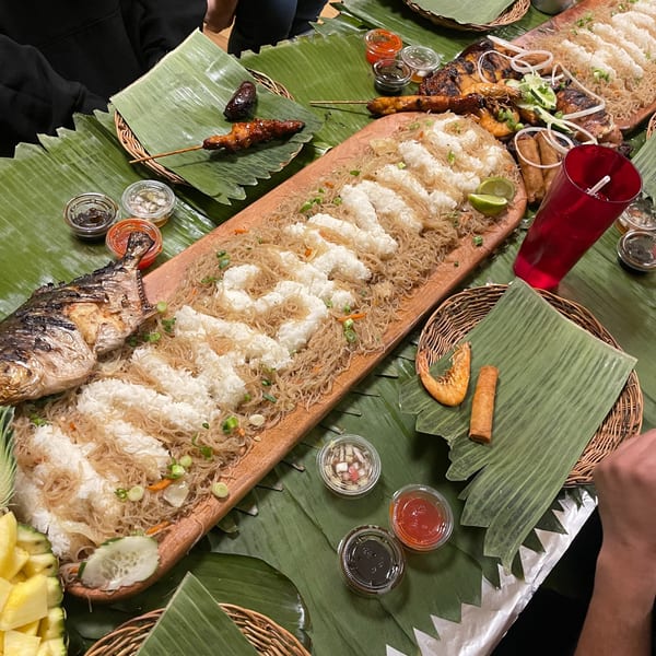A Filipino boodle fight feast with grilled fish, skewers, noodles, rice, and sauces on banana leaves.