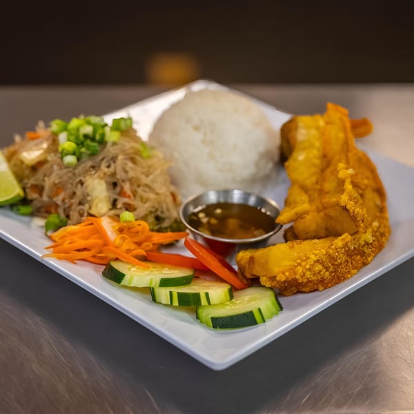Filipino dish with pancit, white rice, fried chicken, and a side of sliced cucumbers and carrots.