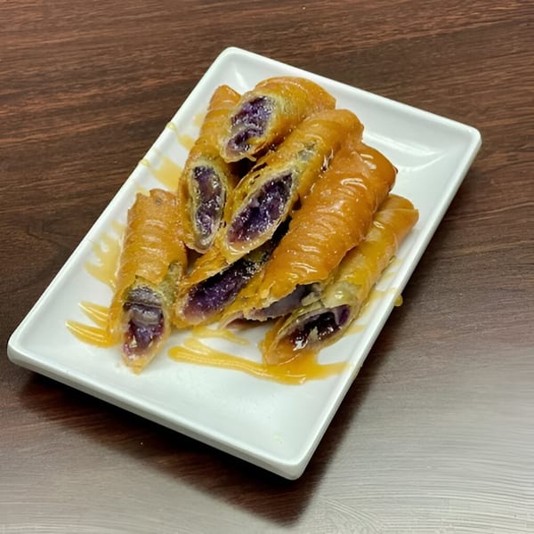 Golden-fried Filipino turon with purple ube filling, drizzled with honey on a white rectangular plate.